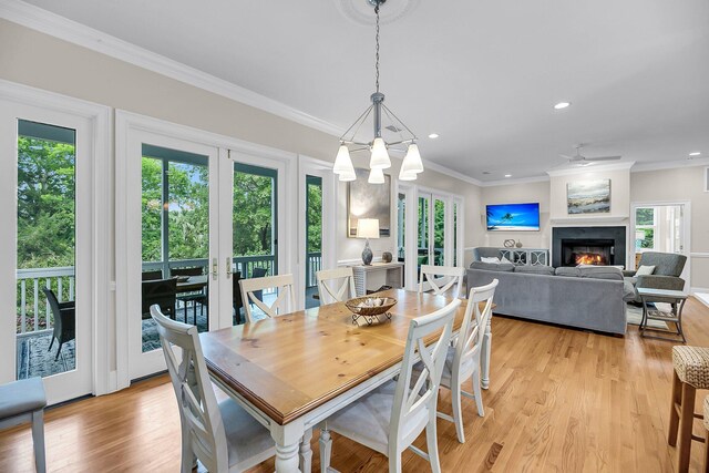 dining area featuring a lit fireplace, light wood-type flooring, recessed lighting, ornamental molding, and french doors