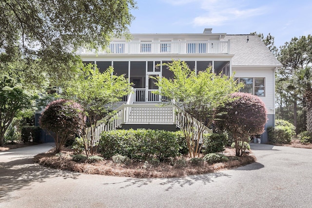 view of front of home featuring stairs, a sunroom, roof with shingles, and a balcony