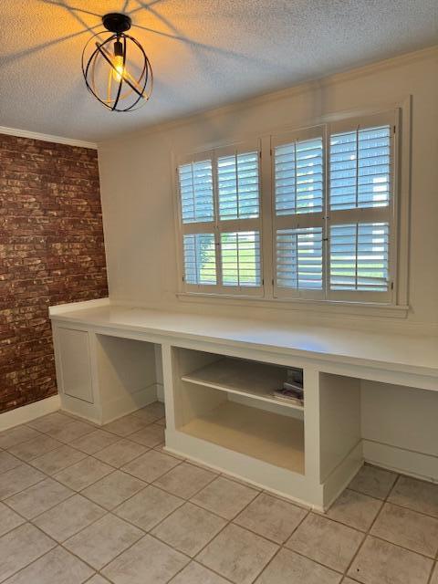 1129 Levi St, Manning, SC 29102 - unfurnished dining area with light tile patterned floors, brick wall, a textured ceiling, crown molding, and baseboards
