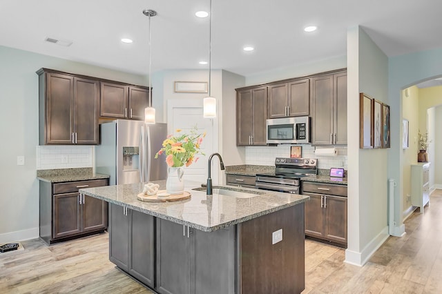 kitchen featuring light stone counters, a sink, arched walkways, backsplash, and stainless steel appliances