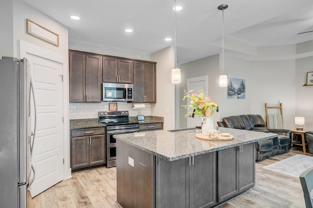 kitchen with light wood finished floors, a center island, a sink, light stone countertops, and appliances with stainless steel finishes