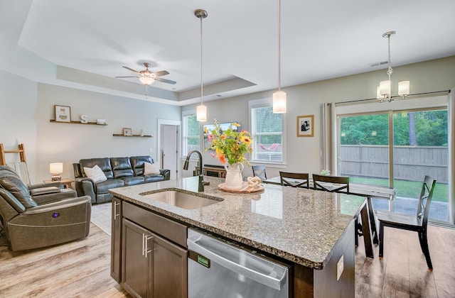 kitchen featuring light wood-style flooring, a tray ceiling, stainless steel dishwasher, a sink, and open floor plan