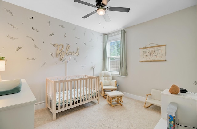 carpeted bedroom with ceiling fan, baseboards, and a crib