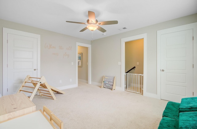 interior space featuring a ceiling fan, baseboards, carpet flooring, visible vents, and an upstairs landing