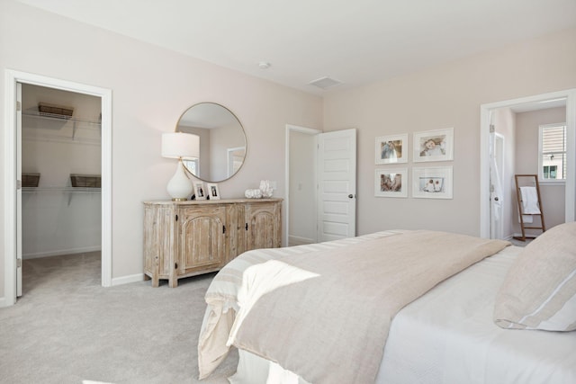 bedroom featuring a walk in closet, light colored carpet, a closet, and baseboards