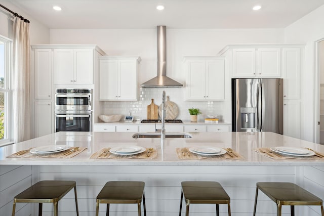 kitchen featuring a spacious island, tasteful backsplash, white cabinetry, appliances with stainless steel finishes, and wall chimney range hood