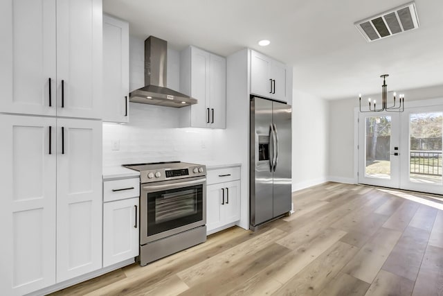 kitchen featuring light wood finished floors, visible vents, appliances with stainless steel finishes, white cabinets, and wall chimney range hood