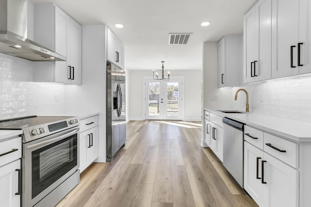 kitchen featuring french doors, stainless steel appliances, light countertops, a sink, and wall chimney exhaust hood