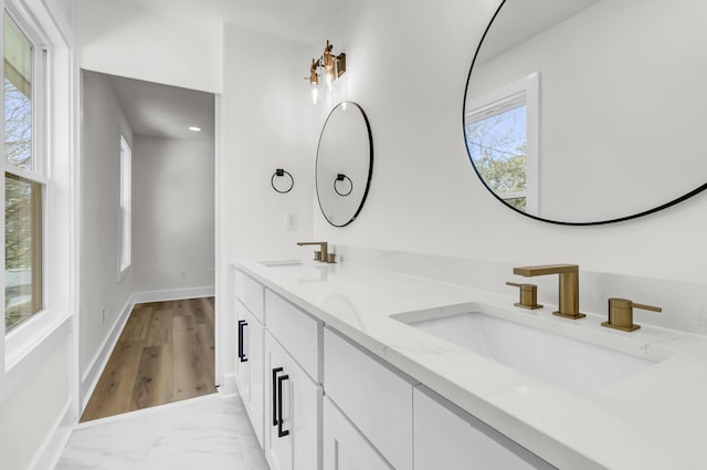 bathroom with marble finish floor, double vanity, a sink, and baseboards