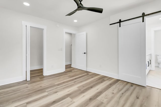 unfurnished bedroom featuring light wood finished floors, a barn door, baseboards, and recessed lighting