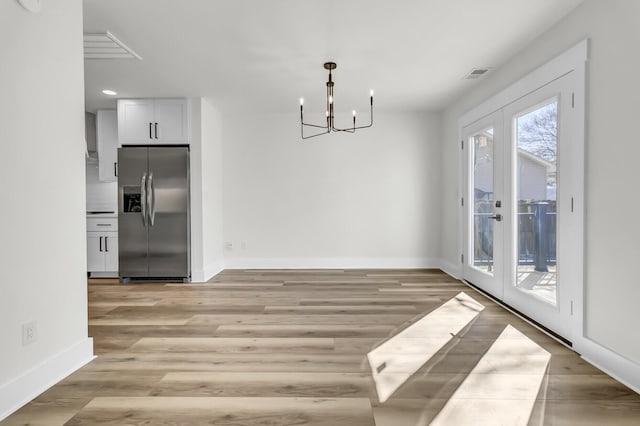 unfurnished dining area featuring french doors, visible vents, light wood-style floors, a chandelier, and baseboards