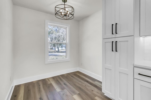 unfurnished dining area with a chandelier, wood finished floors, and baseboards