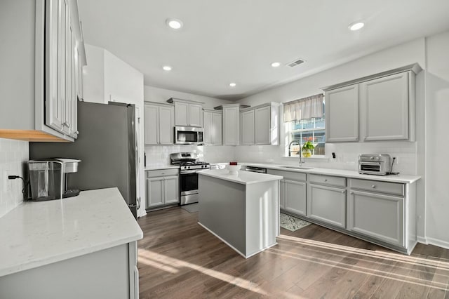 kitchen with gray cabinets, appliances with stainless steel finishes, sink, a center island, and light stone counters