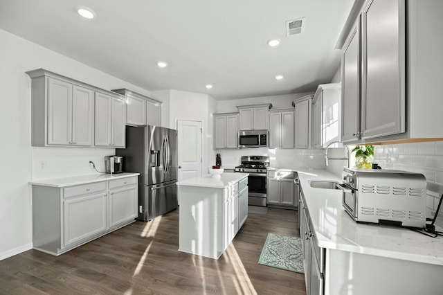 kitchen with a center island, dark hardwood / wood-style floors, gray cabinets, stainless steel appliances, and decorative backsplash