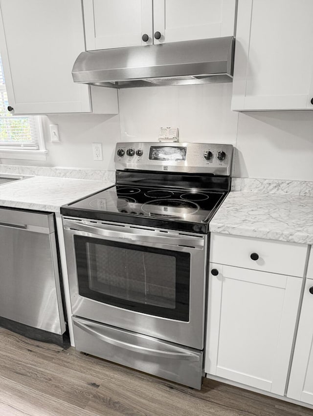 kitchen featuring wood-type flooring, light stone countertops, stainless steel appliances, and white cabinetry