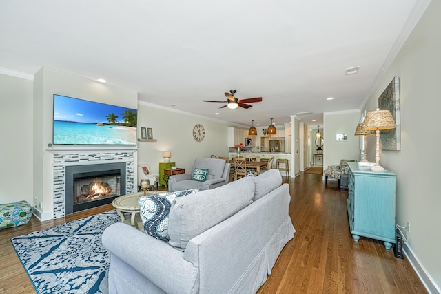 living room featuring hardwood / wood-style floors, ceiling fan, ornamental molding, and a tile fireplace