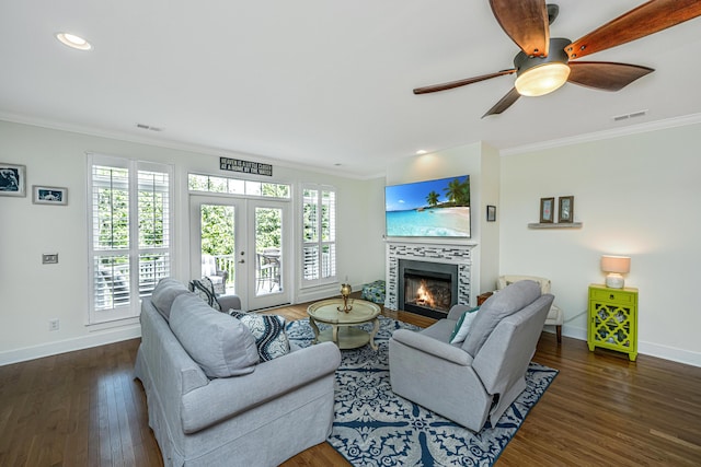 living room with french doors, ceiling fan, ornamental molding, dark hardwood / wood-style flooring, and a tiled fireplace