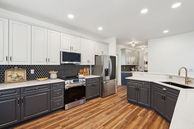 kitchen featuring sink, white cabinetry, stainless steel appliances, light hardwood / wood-style floors, and backsplash