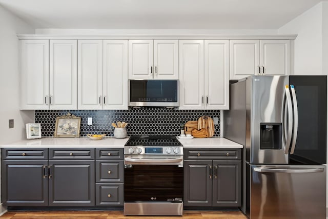 kitchen with gray cabinets, appliances with stainless steel finishes, white cabinetry, decorative backsplash, and light hardwood / wood-style floors