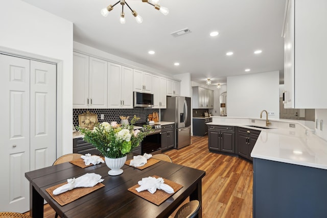 kitchen featuring appliances with stainless steel finishes, sink, backsplash, white cabinets, and light hardwood / wood-style floors