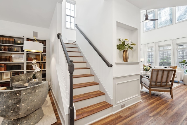 stairs with ceiling fan, a towering ceiling, and wood-type flooring