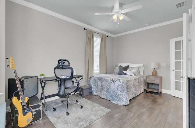 bedroom featuring wood finished floors, a ceiling fan, visible vents, baseboards, and ornamental molding