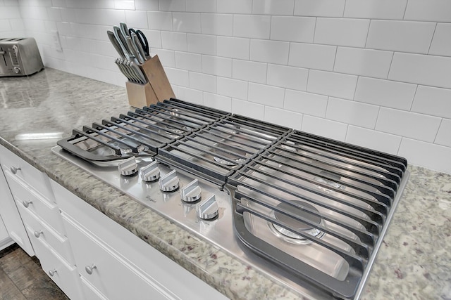 interior details featuring stainless steel gas cooktop, backsplash, white cabinetry, and light stone countertops