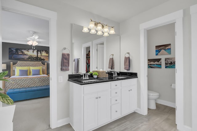 ensuite bathroom with double vanity, baseboards, toilet, ceiling fan, and a sink