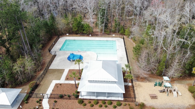 community pool featuring playground community, fence, and a wooded view