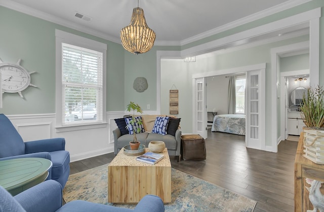 living area with a chandelier, hardwood / wood-style flooring, a wainscoted wall, visible vents, and crown molding