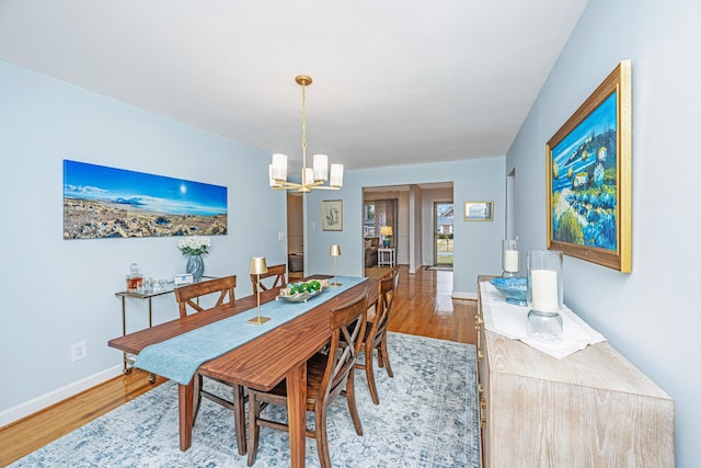 dining space with light wood finished floors, baseboards, and an inviting chandelier