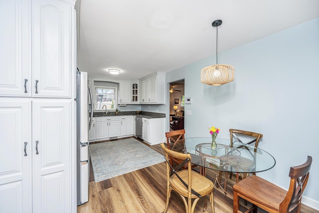 kitchen featuring dark countertops, appliances with stainless steel finishes, white cabinets, a sink, and wood finished floors