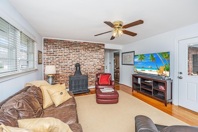 living room featuring ceiling fan, brick wall, wood finished floors, and a wood stove