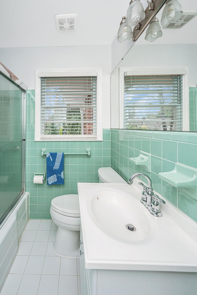 bathroom with tile walls, bath / shower combo with glass door, toilet, vanity, and tile patterned floors