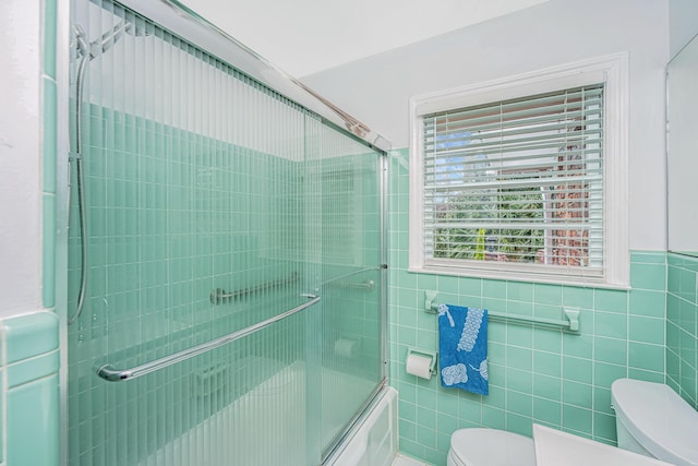 full bath featuring wainscoting, enclosed tub / shower combo, tile walls, and toilet