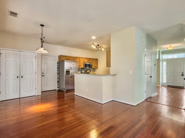 kitchen featuring kitchen peninsula, tasteful backsplash, stainless steel appliances, dark wood-type flooring, and decorative light fixtures