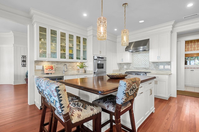 kitchen featuring white cabinetry, decorative light fixtures, light wood-type flooring, double oven, and wall chimney range hood