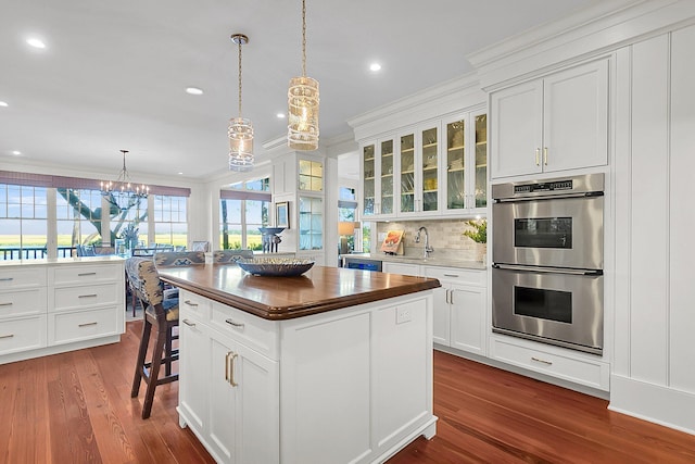 kitchen with a kitchen island, a breakfast bar, double oven, white cabinetry, and hanging light fixtures