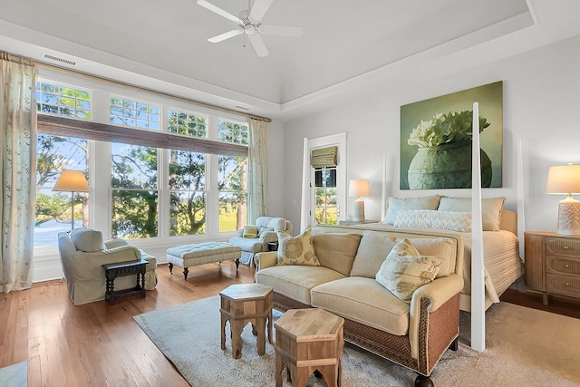 bedroom featuring hardwood / wood-style flooring, ceiling fan, a tray ceiling, and multiple windows