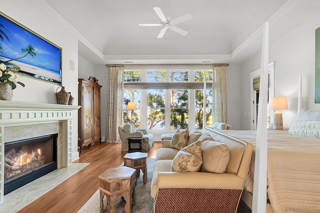 bedroom with ceiling fan, a high end fireplace, a tray ceiling, and light hardwood / wood-style floors