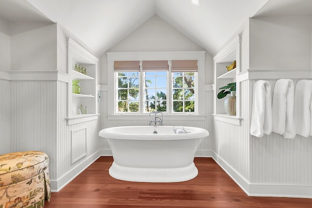 bathroom with built in shelves, wood-type flooring, a bathing tub, and vaulted ceiling