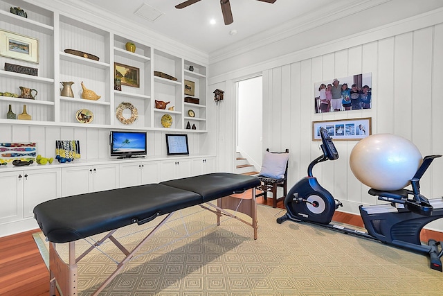 workout area with ornamental molding, built in features, ceiling fan, and light hardwood / wood-style flooring