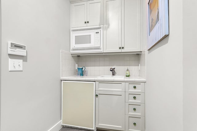 bar featuring tasteful backsplash, sink, tile counters, and white microwave