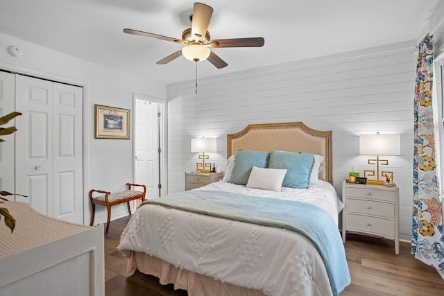 bedroom with wood walls, ceiling fan, a closet, and light hardwood / wood-style flooring