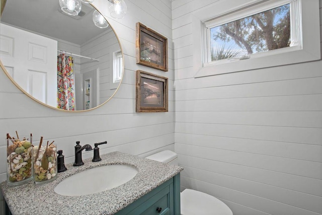 bathroom featuring toilet, wood walls, vanity, and curtained shower