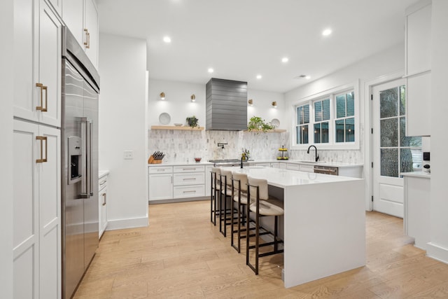 kitchen with tasteful backsplash, open shelves, a sink, light wood-style flooring, and appliances with stainless steel finishes
