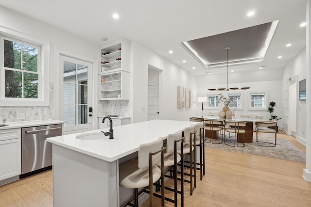kitchen featuring dishwasher, a raised ceiling, a sink, and light wood-style flooring