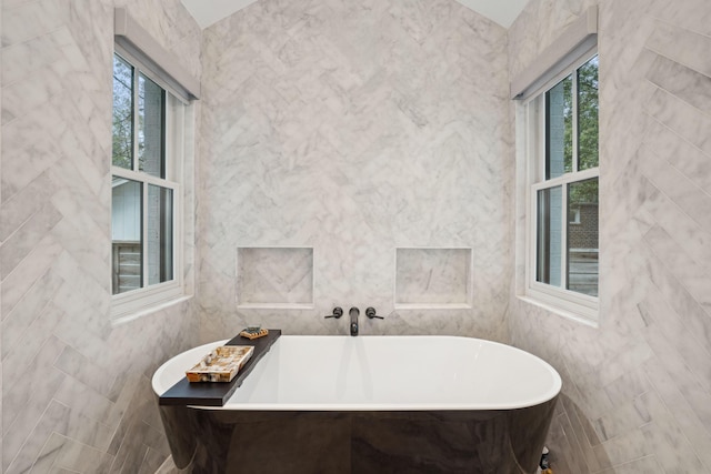 full bathroom featuring a freestanding bath, tile walls, and a wealth of natural light