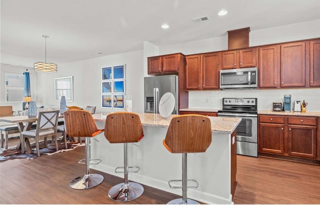 kitchen with appliances with stainless steel finishes, pendant lighting, backsplash, a kitchen bar, and light stone counters