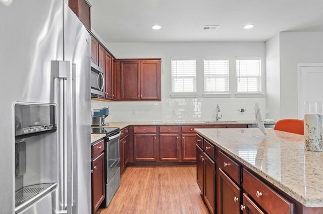 kitchen featuring sink, light hardwood / wood-style flooring, appliances with stainless steel finishes, backsplash, and light stone countertops